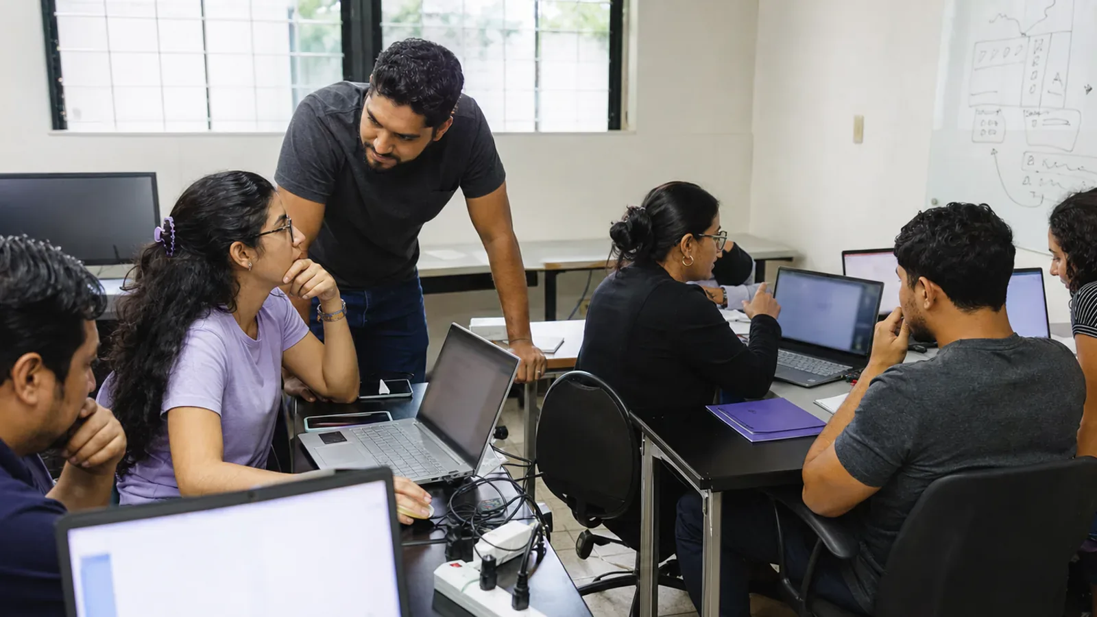 A coding mentor supports two groups of learners during a practical programming lab.