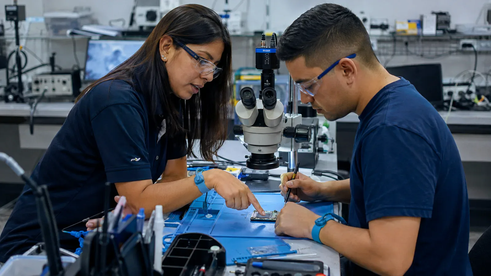 Instructora guía una práctica segura de reparación de celulares bajo microscopio.