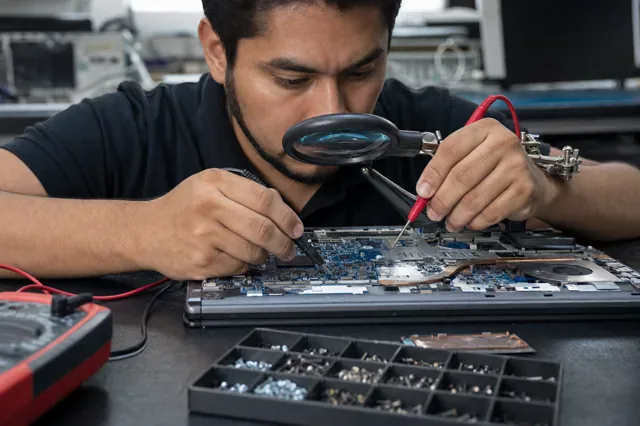 Técnico mide la placa de una laptop abierta con un multímetro.