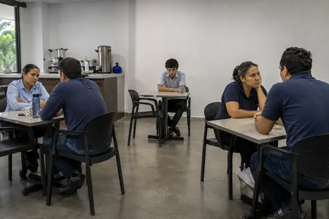 Empleado permanece aislado entre grupos tensos en el comedor del personal.