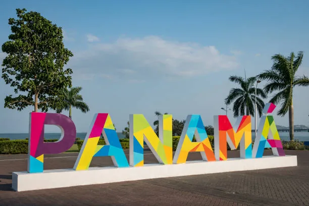 Colorful "PANAMÁ" sign with palm trees and ocean in background under a blue sky.