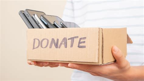 Person holding a cardboard box labeled "DONATE" filled with multiple mobile phones for donation or recycling.