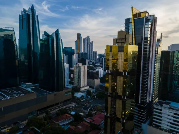 Aerial view of modern skyscrapers in Panama City, featuring blue and gold glass buildings under a cloudy sky.