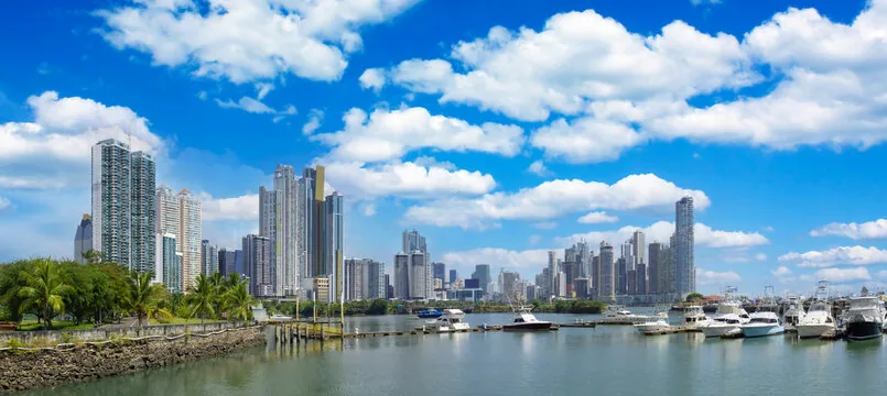 Panoramic view of Panama City with skyscrapers, palm trees, and boats on the water under a blue sky with clouds.
