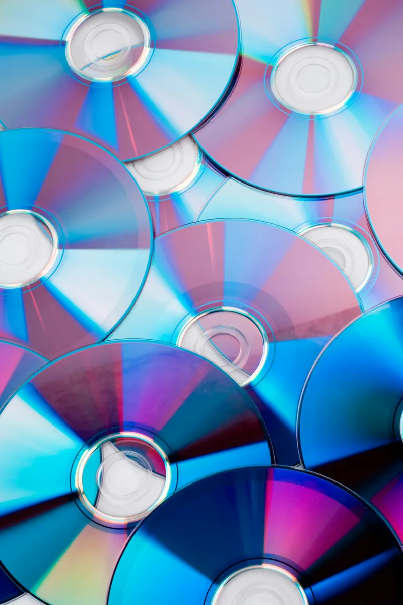 Stack of CD/DVDs with iridescent reflections in blue, purple, and pink hues, forming an abstract pattern.