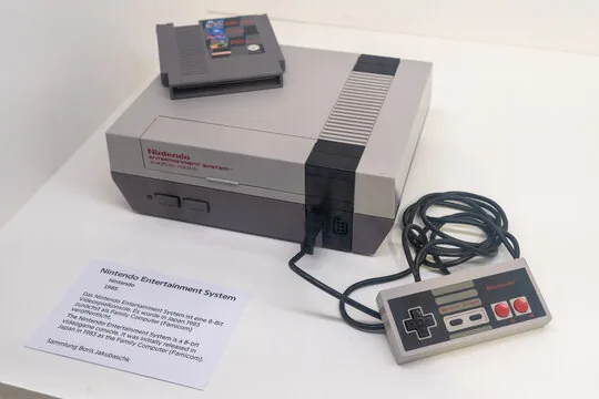 Gray Nintendo Entertainment System (NES) console with cartridge and controller on a white surface.