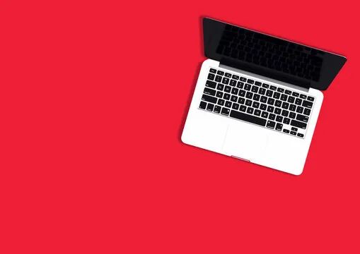 Open silver laptop with black screen on bright red background, aerial view.