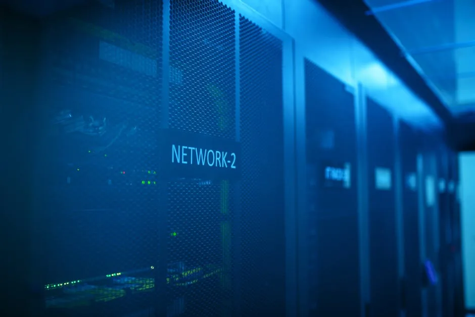 Close-up of server racks in a data center, bathed in blue light. A rack is labeled 'NETWORK-2' with blinking green lights.