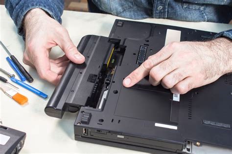 Man repairing a laptop, inserting or removing the battery. Repair tools on the table.