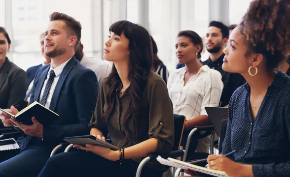 Diverse group of attentive professionals at a conference or seminar, taking notes and actively listening.