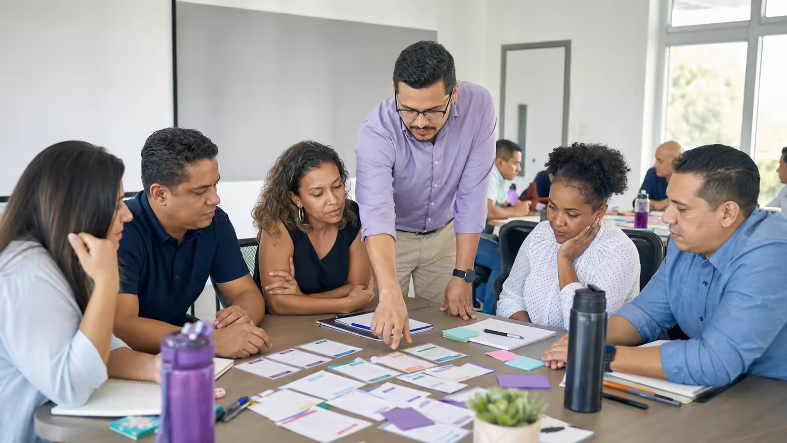 Un facilitador guía a un grupo diverso de personas adultas durante un taller práctico en equipo.