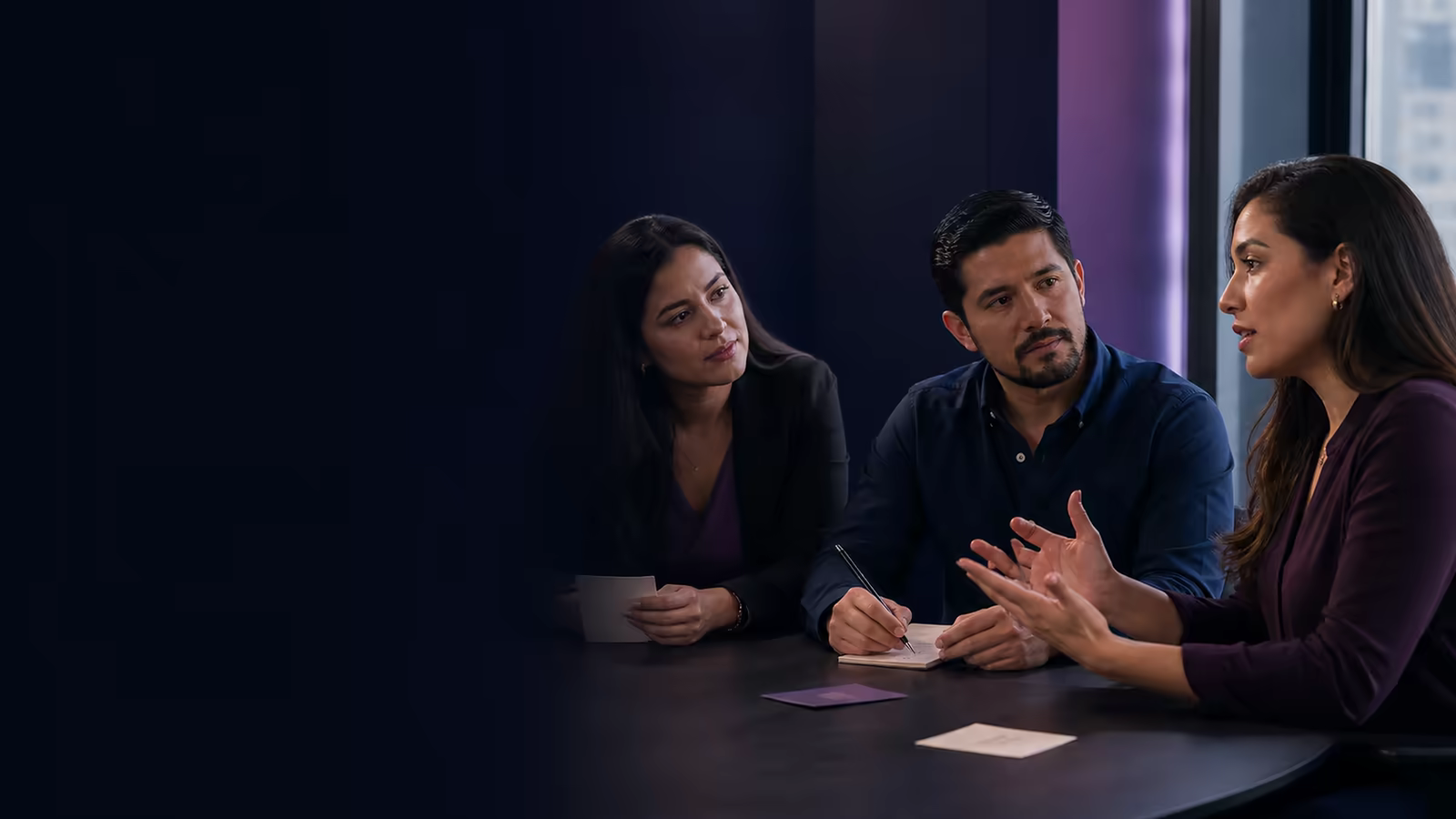 Tres profesionales latinoamericanos practican una conversación asertiva mientras escuchan, explican y toman notas.