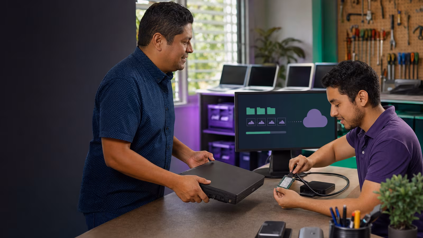 Un técnico de Crezendo recupera archivos de una laptop mientras su donante entrega la computadora para reutilización educativa.